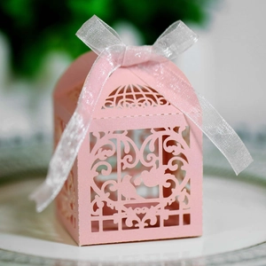 Detail of pink laser-cut wedding favor box with bird pattern and white organza ribbon