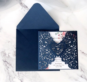 Detail of laser-cut navy invitation with floral pattern and insert on marble background