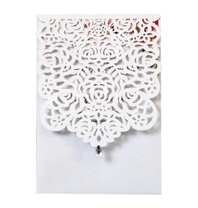 Close-up of laser-cut white rose wedding invitation with a crystal droplet pendant