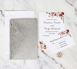 Detailed view of laser-cut glitter wedding invitation set with floral motifs and envelopes