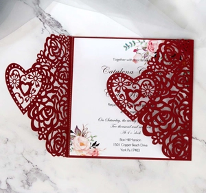 Detail of laser-cut burgundy rose and heart wedding invitation on marble background