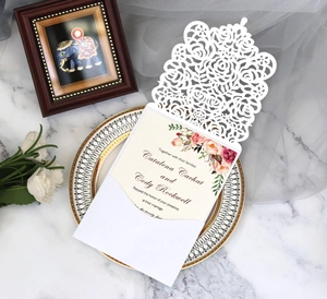 Detail of laser cut white rose wedding invitation with floral insert and matching envelope