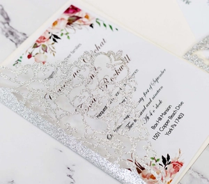 Close-up of laser-cut silver glitter wedding invitation with elegant floral inner card