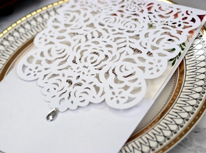 Close-up of laser cut white rose wedding invitation cover with elegant rhinestone detail