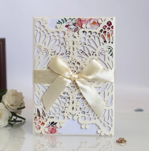 Detail of laser-cut wedding invitation with cream ribbon bow and floral inner card