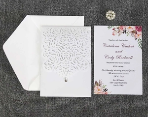 Detail of laser-cut white wedding invitation with floral insert and pearl brooch