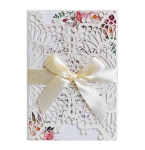 Detail of laser-cut ivory wedding invitation with silk bow and floral inner page