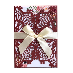 Intricate laser-cut burgundy wedding invitation with champagne ribbon and floral inner card