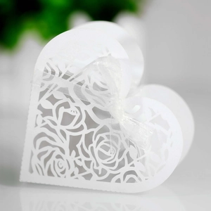 Detail of laser-cut heart favor box with intricate rose patterns and white ribbon bow