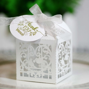 Close-up of laser-cut white favor box with bird patterns, white ribbon and thank you tag