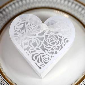 Close-up of white heart-shaped wedding favor box with laser-cut rose patterns and ribbon bow