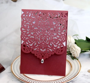 Detailed laser-cut rose pattern on burgundy invitation card with elegant teardrop pendant