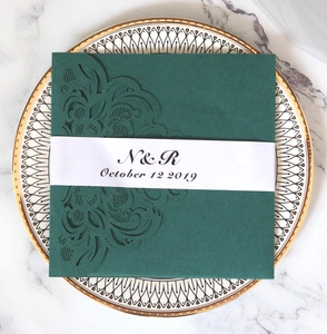 Detail of dark green laser-cut wedding invitation with elegant vine patterns and white belly band