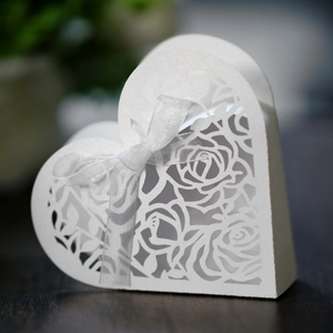 Macro shot of laser-cut white heart favor box with floral patterns and a silk ribbon
