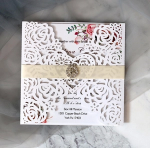Detail view of laser-cut rose invitation with cream ribbon and faux diamond buckle decoration