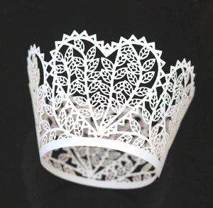 White laser-cut crown cupcake wrapper with intricate leaf patterns on black background