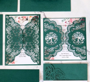 Elegant laser-cut dark green wedding invitation set with floral inner card on marble background