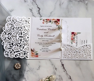 Macro detail of laser-cut white wedding invitation set with intricate floral lace pattern