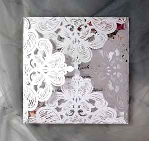 Macro shot of white laser-cut floral square wedding invitation on marble background