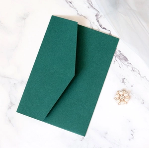 Elegant dark green matte envelope on white marble background with a decorative pearl brooch