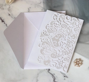 Macro detail of laser-cut white wedding invitation set with elegant floral patterns