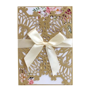 Close-up of laser-cut gold glitter wedding invitation with cream ribbon and floral card