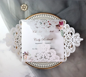 Elegant white laser-cut wedding invitation set with floral card on marble background