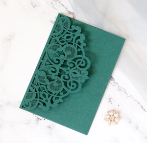 Detailed laser cut dark green invitation envelope with elegant floral patterns on marble