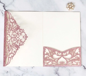 Flat lay of laser-cut rose gold glitter wedding invitation with intricate floral patterns