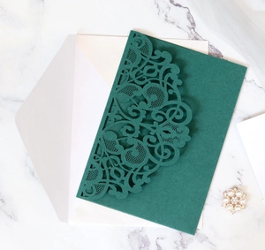 Detailed laser-cut dark green wedding invitation on marble background with white envelope