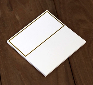 Detail of white place cards with gold foil borders stacked on a textured wood surface