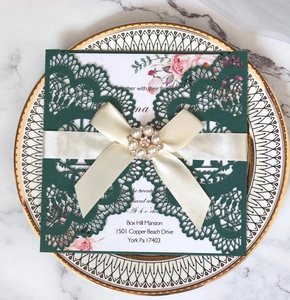 Detail of laser-cut wedding invitation with green hollow cover and pearl ribbon bow