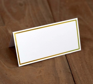 Detailed view of white place card with elegant gold foil borders on a wooden table surface