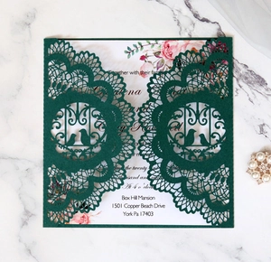 Detail of laser-cut dark green floral wedding invitation with bird motif and white insert card