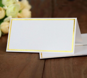 Detail of white place card with gold foil border on a rustic wooden table for weddings
