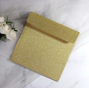 Close-up of elegant gold glitter square envelope on white marble with flowers