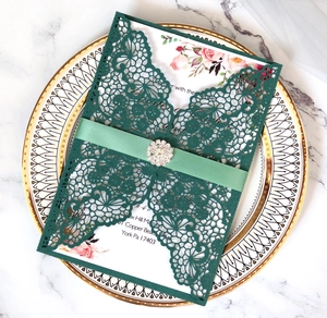 Detail of dark green laser-cut wedding invitation with ribbon and rhinestone buckle