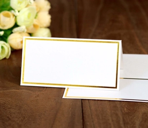 Elegant white wedding place card with gold foil border on a rustic wooden table