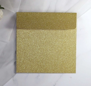 Close-up of square rose gold glitter envelope on white marble and soft fabric background