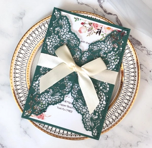 Detail of laser-cut lace invitation with white satin bow on an elegant porcelain plate