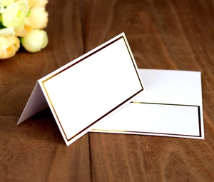 Close-up of white place cards with gold foil borders on a dark wood background