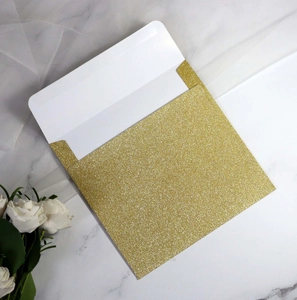 Detailed view of elegant gold glitter envelope on a white marble surface with a white rose
