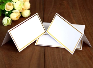 Elegant white place cards with gold foil borders on a wooden table with roses