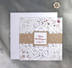 Macro shot of white laser cut wedding invitation with glitter gold band and elegant envelope