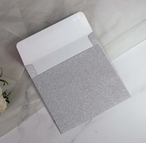 Silver glitter square envelope for wedding invitations on marble background with white flowers