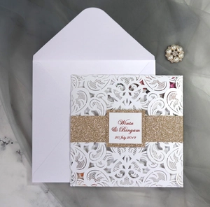 Detail of laser cut white wedding invitation with gold glitter band and floral lace cutout