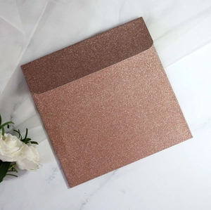 Macro shot of rose gold glitter square envelope on white marble with roses and tulle