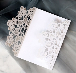 Elegant white laser cut wedding invitation with intricate floral hollow design on marble