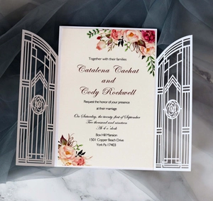 Detailed laser cut tri-fold wedding invitation with elegant rose patterns on marble surface