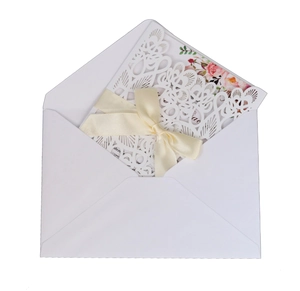 Elegant white laser-cut floral wedding invitation with cream ribbon bow and inner card